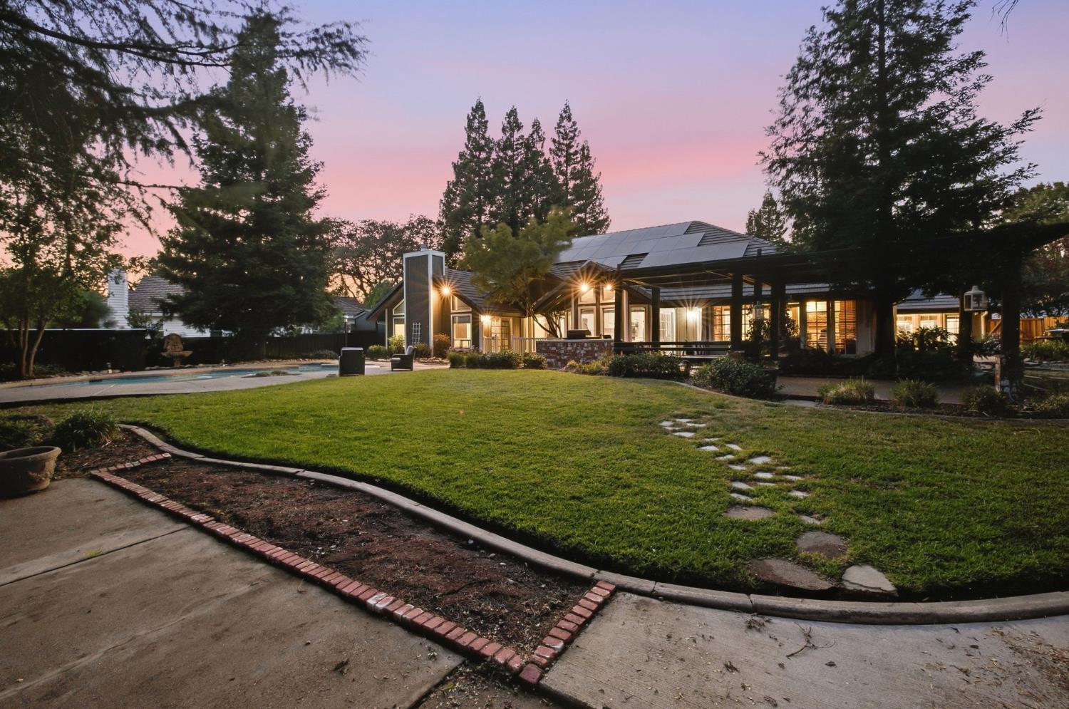 Home with rooftop solar panels, a swimming pool, and covered patio at dusk.