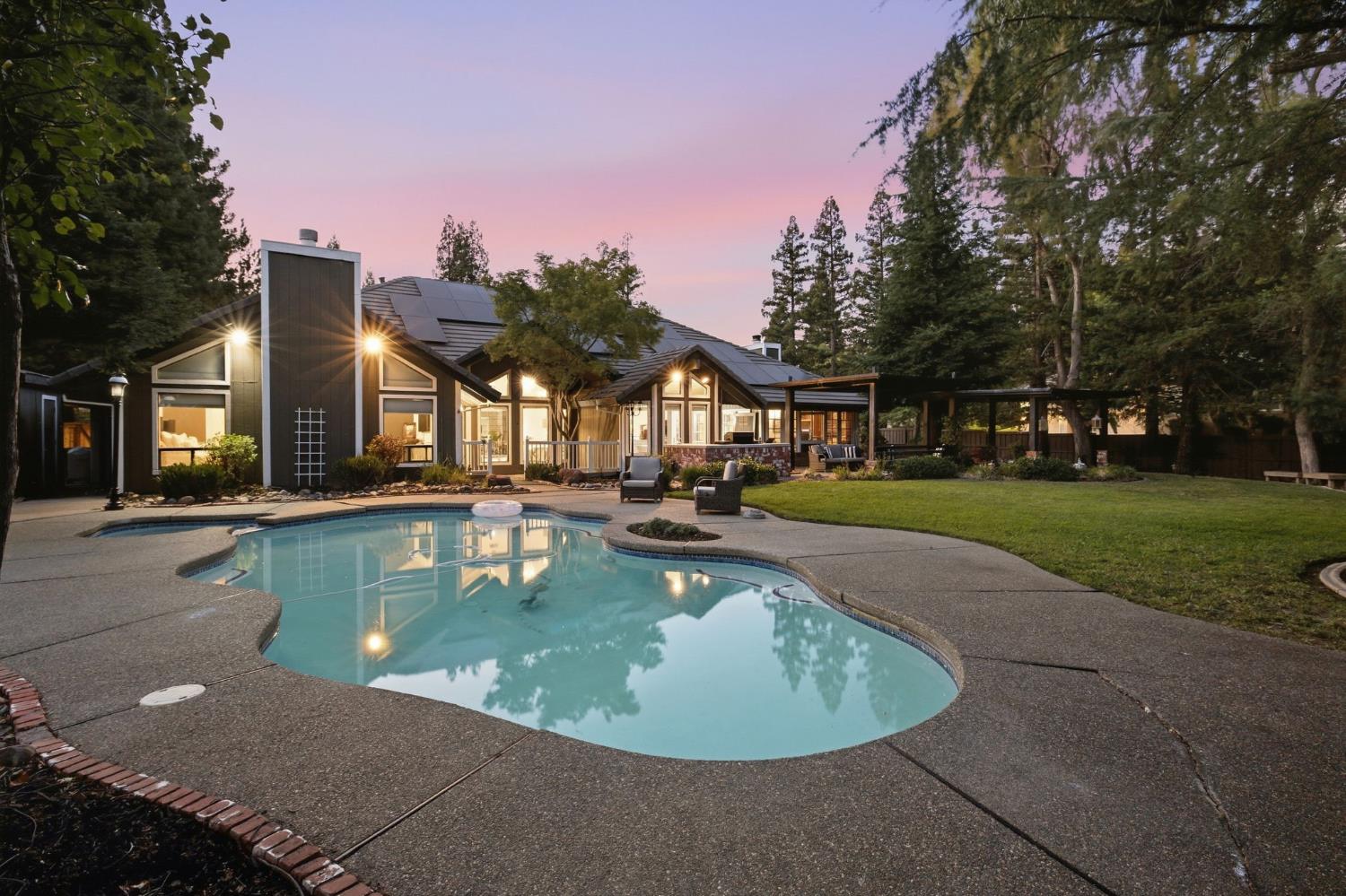 Modern home at dusk with a curved swimming pool and covered patio.