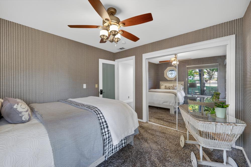 Bedroom with patterned walls, a wood-blade ceiling fan, and a white wicker cart.
