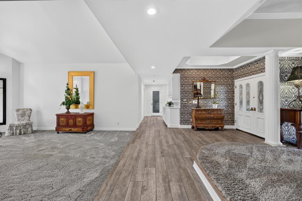 Furnished living area and foyer with patterned wallpaper, wood-look flooring, and white glass-panel double doors.