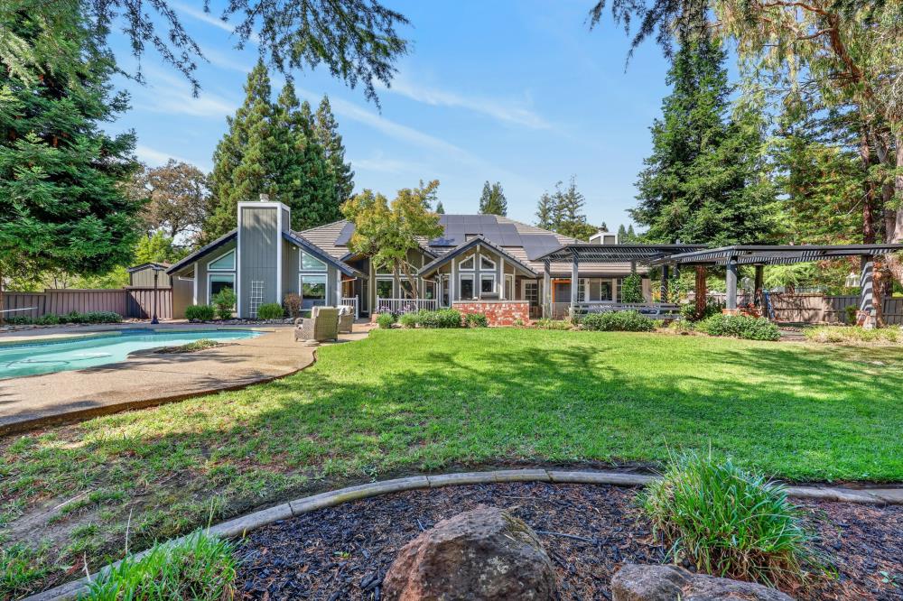 Home’s rear exterior with a swimming pool, covered patio, and spacious lawn.
