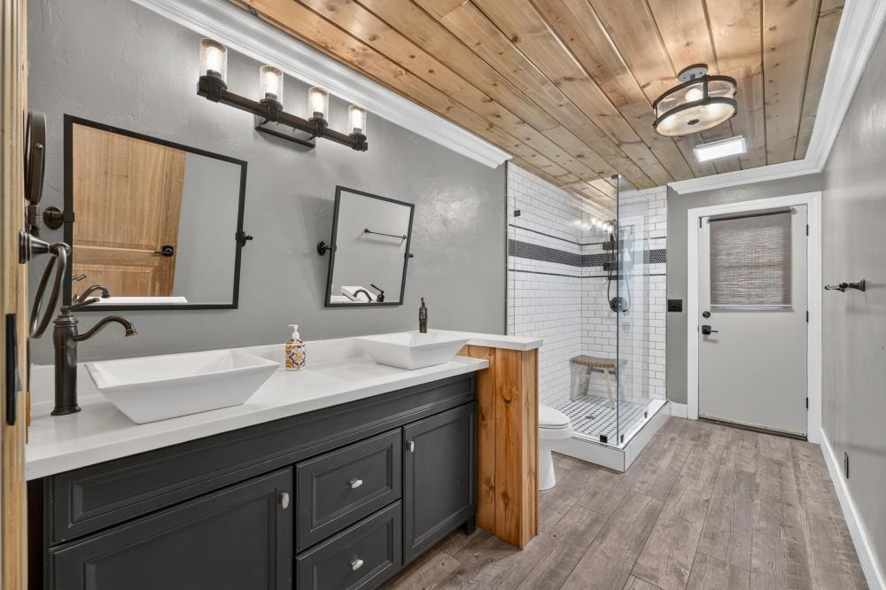 Bathroom with double vessel sinks and a glass shower beneath a wood-plank ceiling.