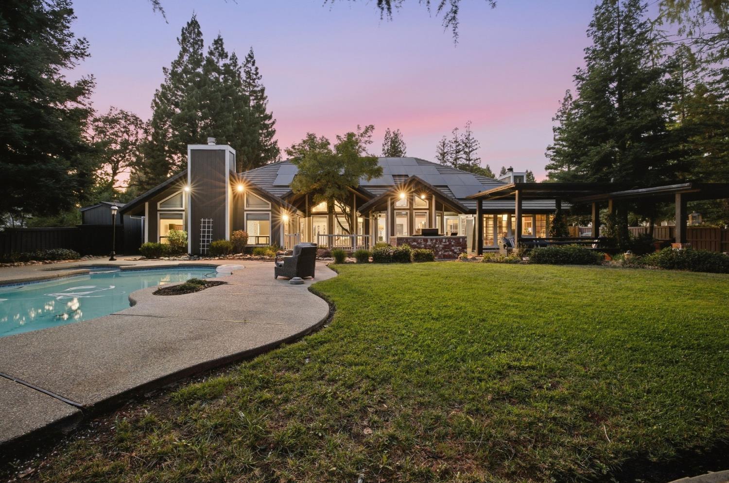 Home rear exterior with a pool, covered patio, and landscaped lawn at dusk.