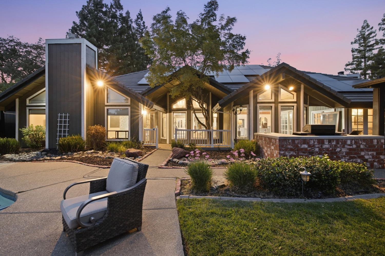 Modern home at dusk with glowing windows, solar panels, landscaped patio, and swimming pool.
