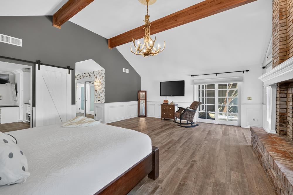 Spacious bedroom with exposed ceiling beams, brick fireplace, and sliding glass doors.