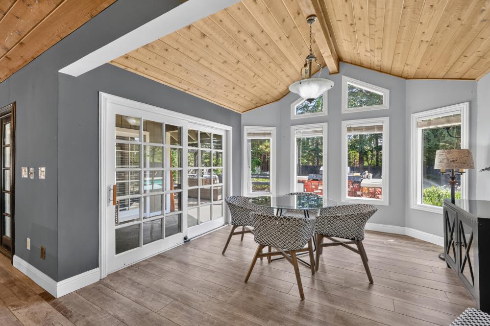 Dining room with a round glass table, tall windows, sliding doors, and a vaulted wood ceiling.