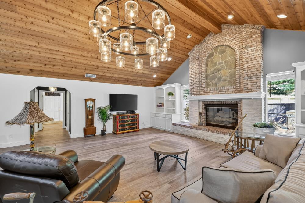 Living room with a vaulted wood ceiling, stone fireplace, and large circular chandelier.