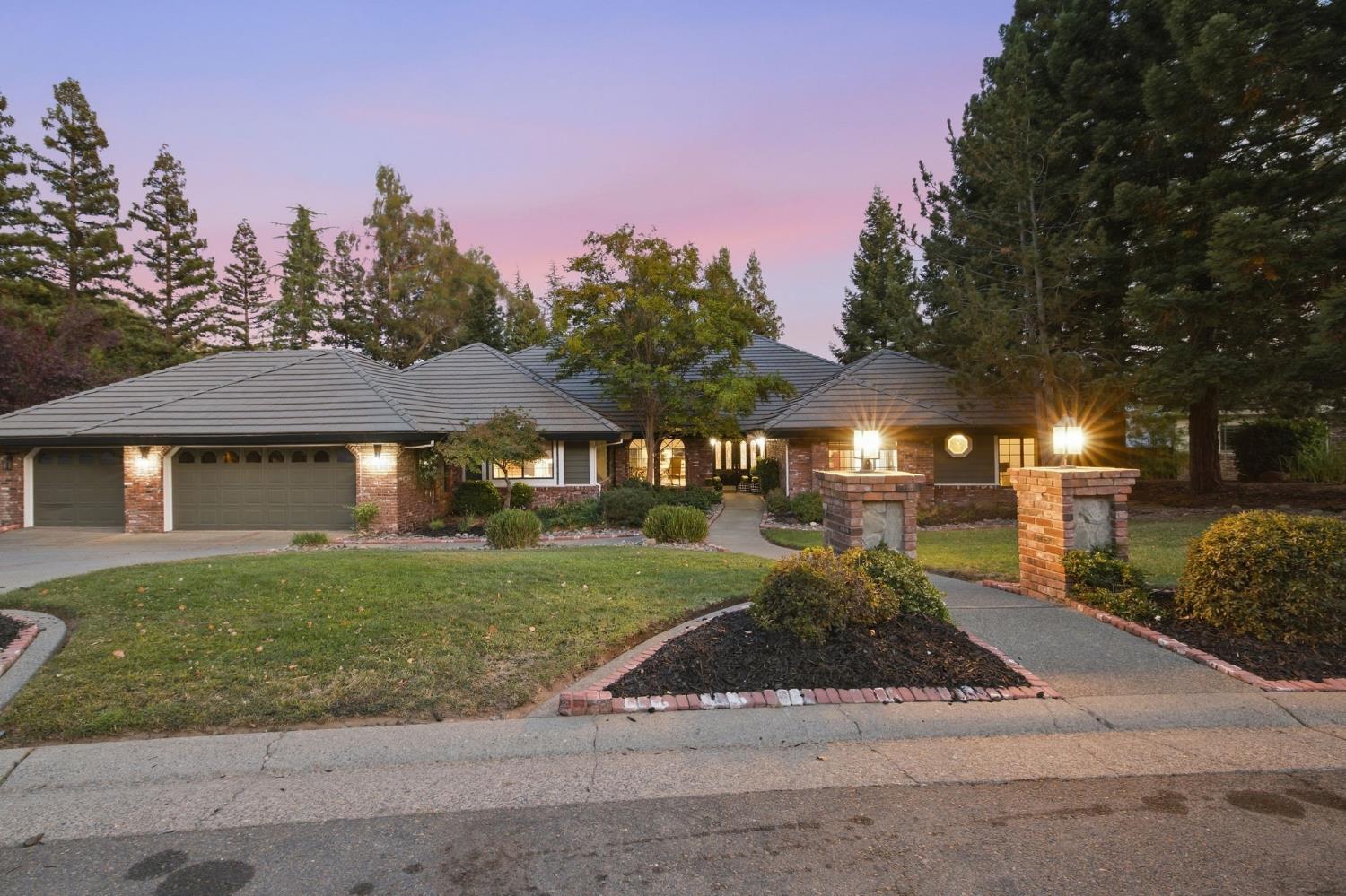 Single-story home with brick accents, lit entry, attached garages, and landscaped driveway at dusk.