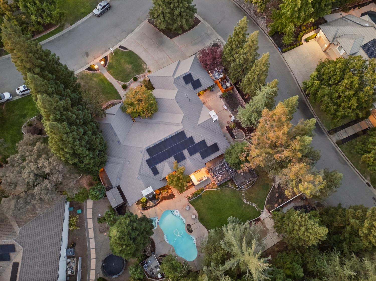 Aerial view of a home with rooftop solar panels, mature trees, and a backyard pool.