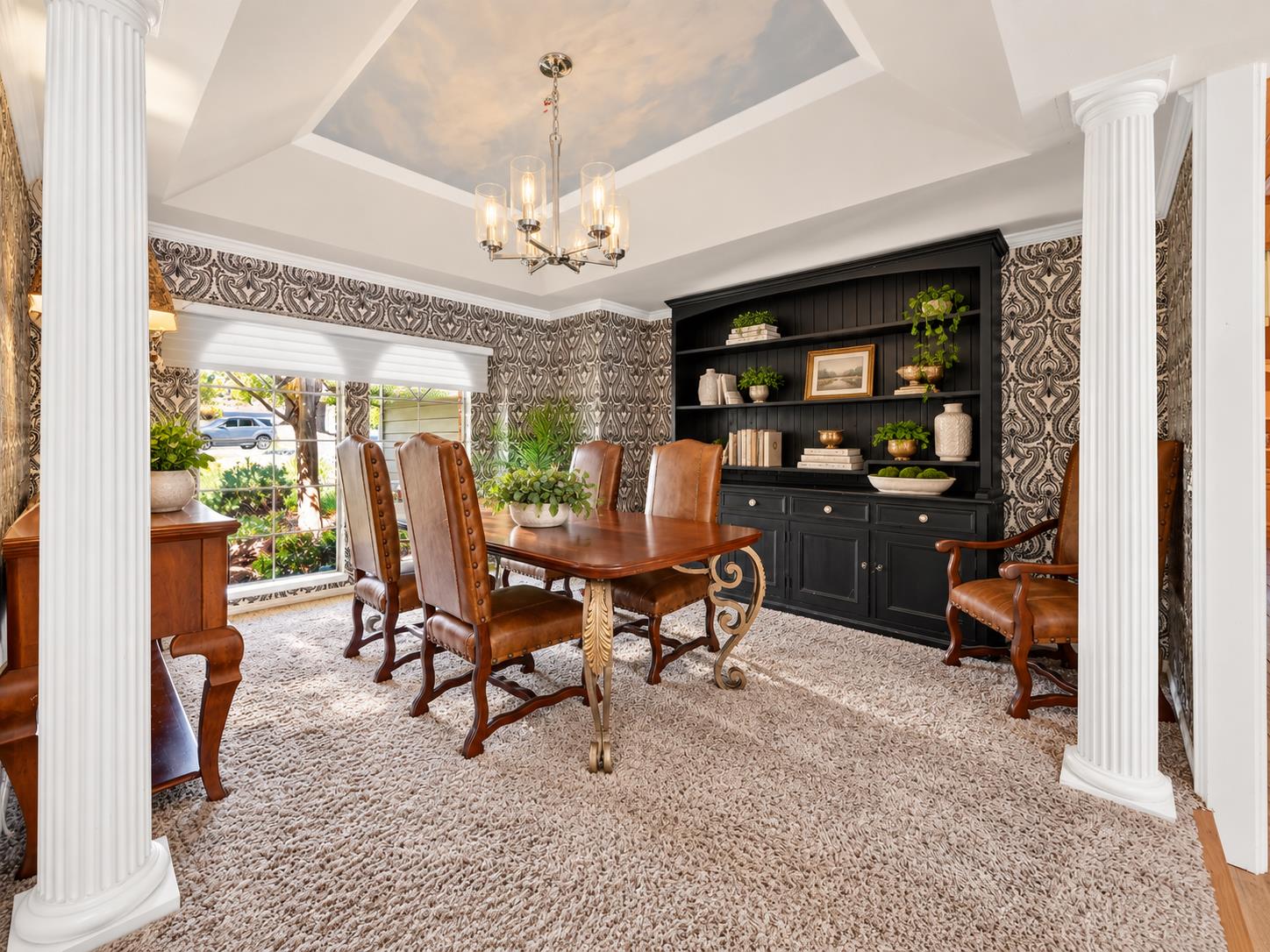 Dining room with a wooden table, leather chairs, ornate wallpaper, and a black built-in hutch.