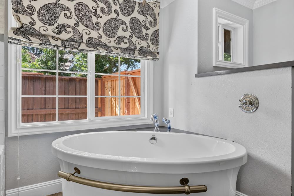 Bathroom with a white freestanding tub beneath a window with a patterned Roman shade.