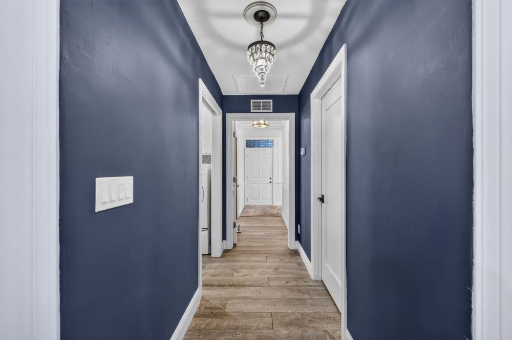 Hallway with dark blue walls, wood-look tile flooring, and a crystal chandelier.
