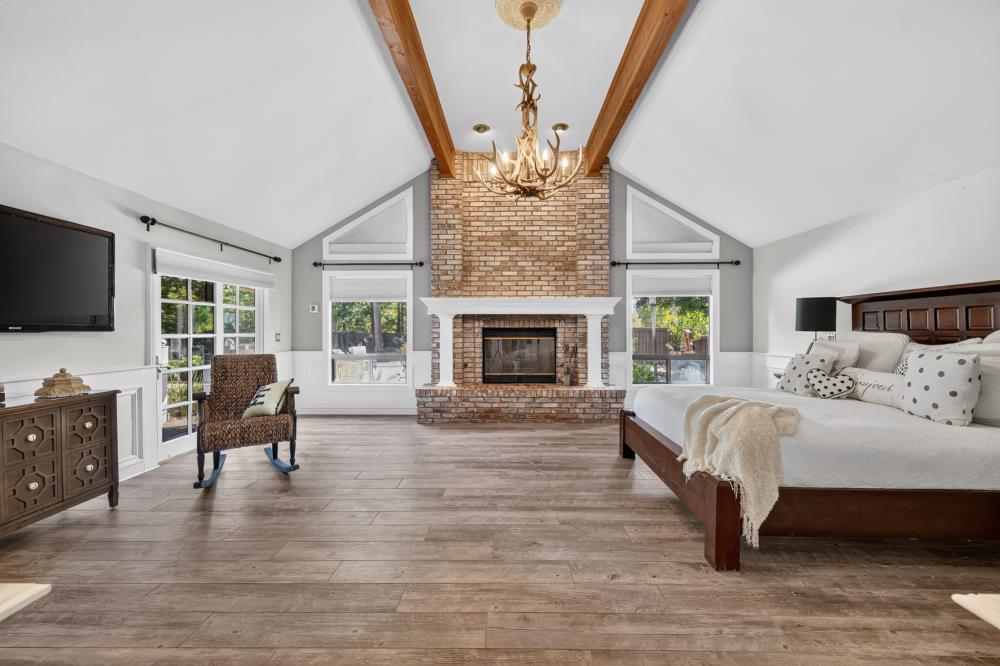 Bedroom with a brick fireplace, vaulted wood-beam ceiling, and large bed.