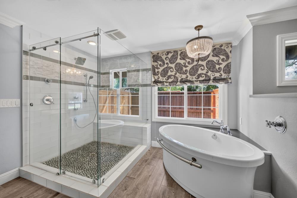 Bathroom with a glass-enclosed shower and freestanding soaking tub beneath a patterned window shade.