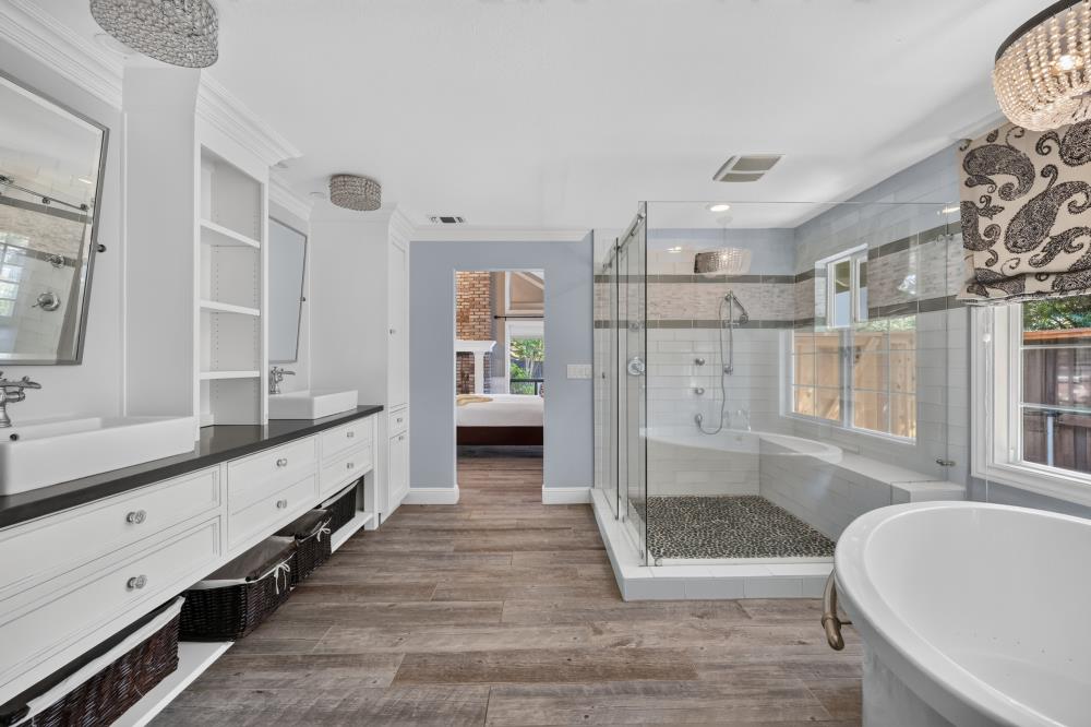Primary bathroom with a long double vanity, glass shower, and freestanding soaking tub.