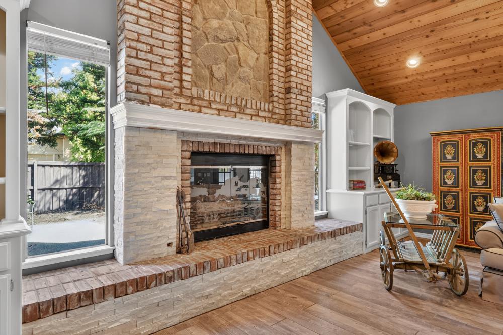 Living room with a large stone fireplace, raised brick hearth, and vaulted wood ceiling.