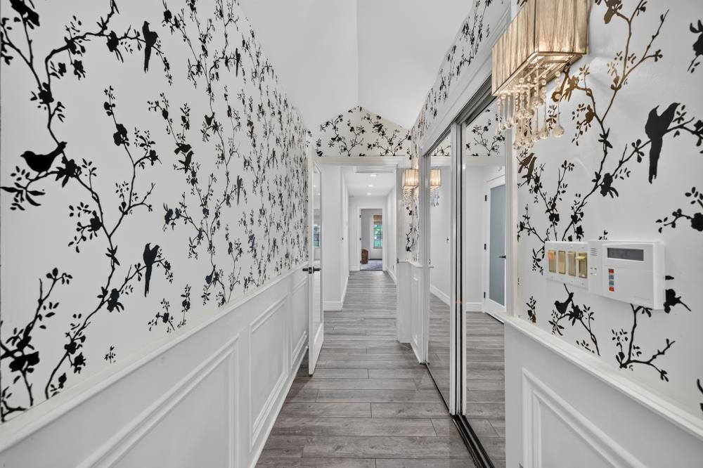 Hallway with black botanical wallpaper, white wainscoting, gray plank flooring, and mirrored closet doors.