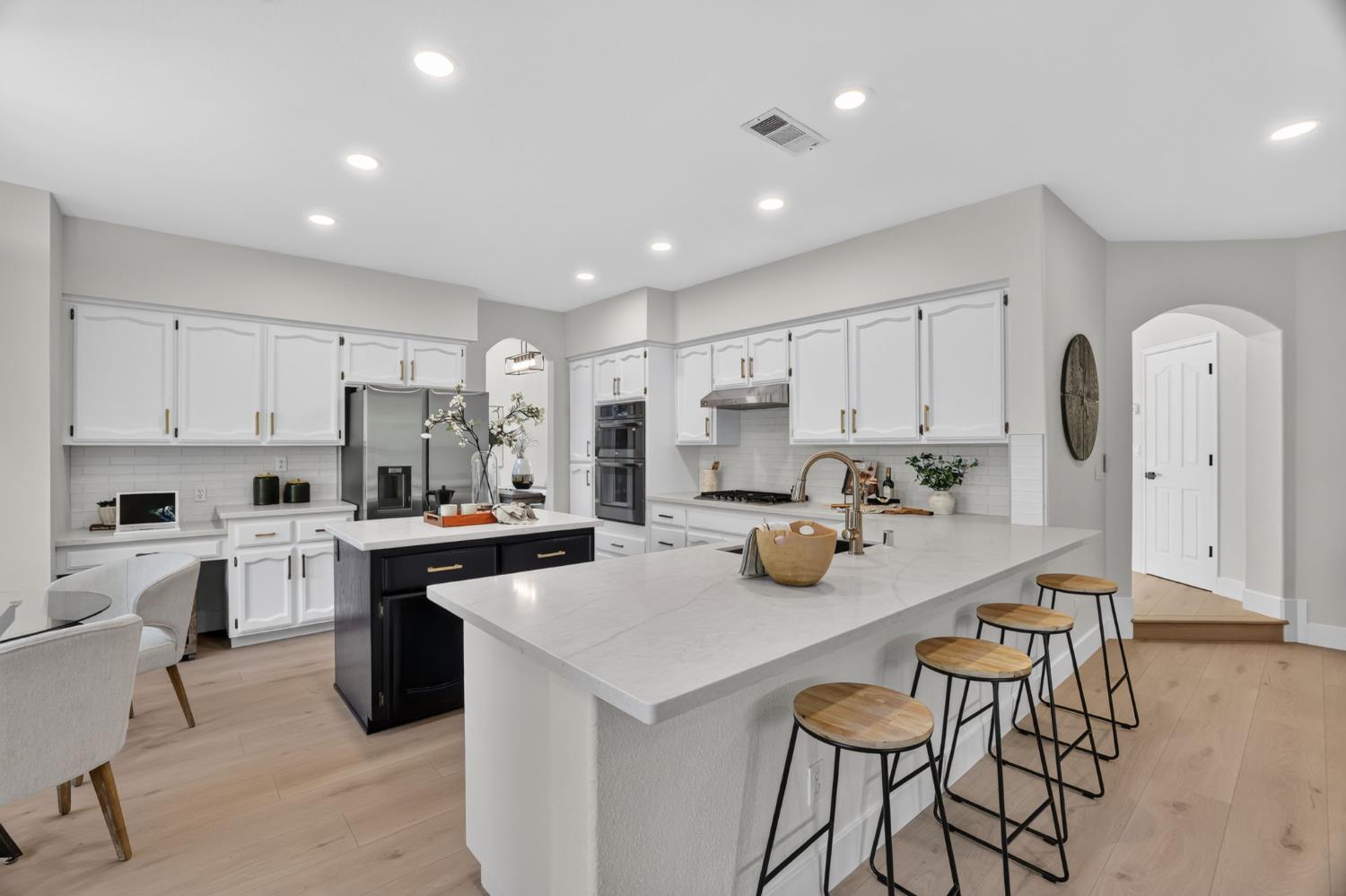 Kitchen with white cabinets, a dark island, and a large peninsula with bar stools.
