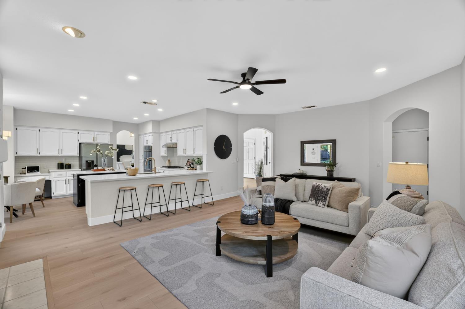 Open-plan living room and kitchen with white cabinetry, island seating, and neutral furnishings.