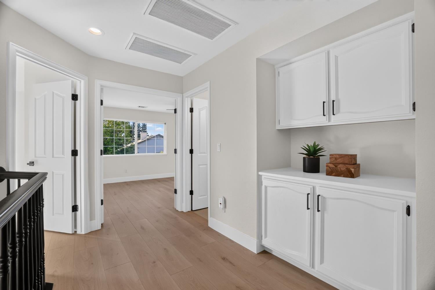 Upstairs hallway with white built-in cabinets, light wood floors, and a doorway to a windowed room.