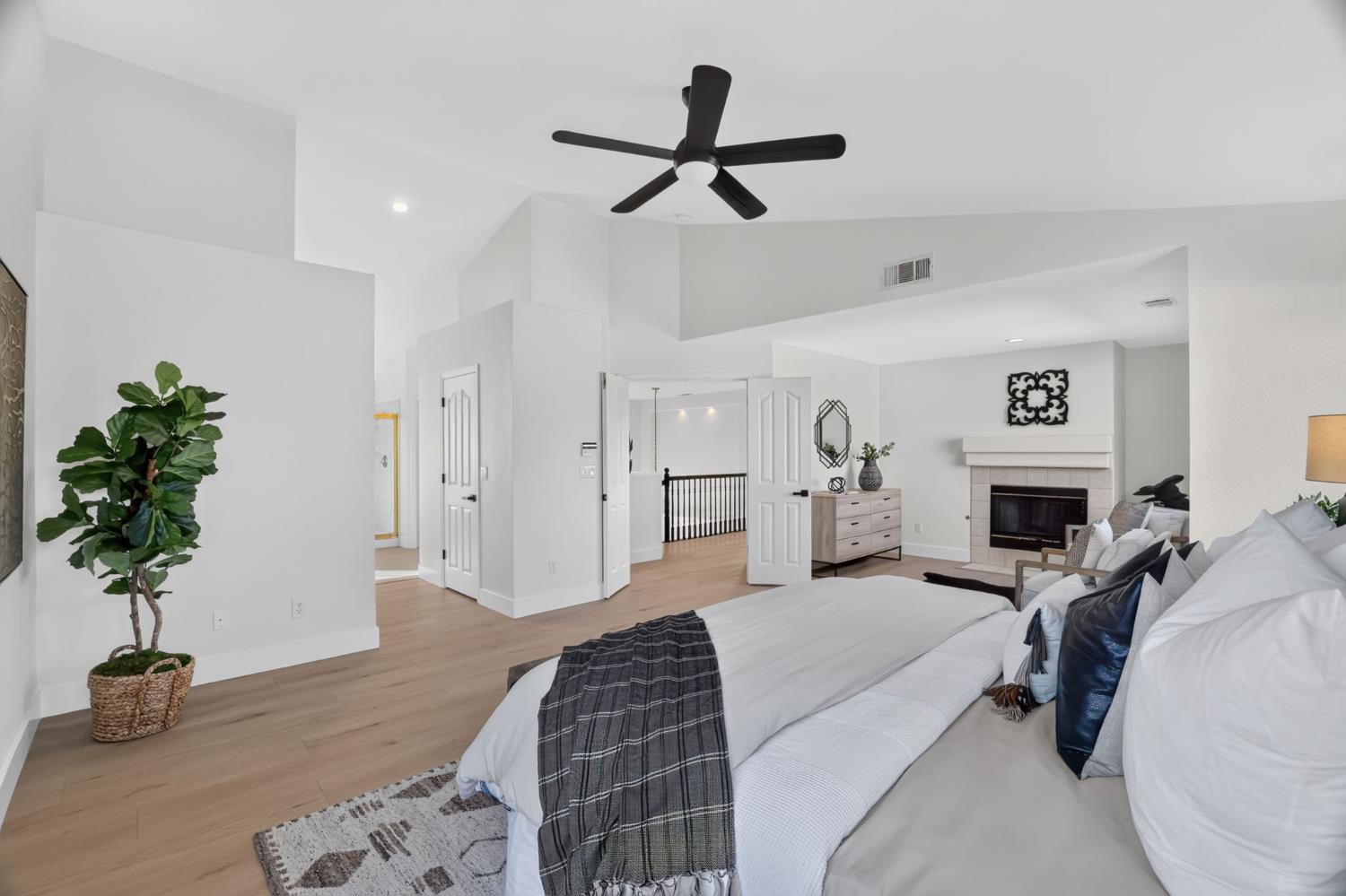 Staged bedroom with a white bed, black ceiling fan, and fireplace.