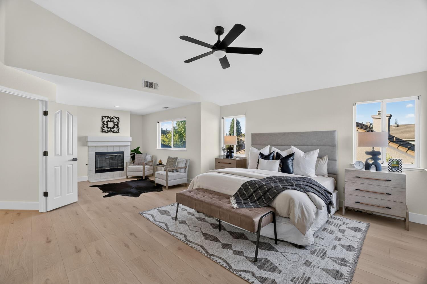 Staged bedroom with a king-size bed, vaulted ceiling, and fireplace beside a sitting area.