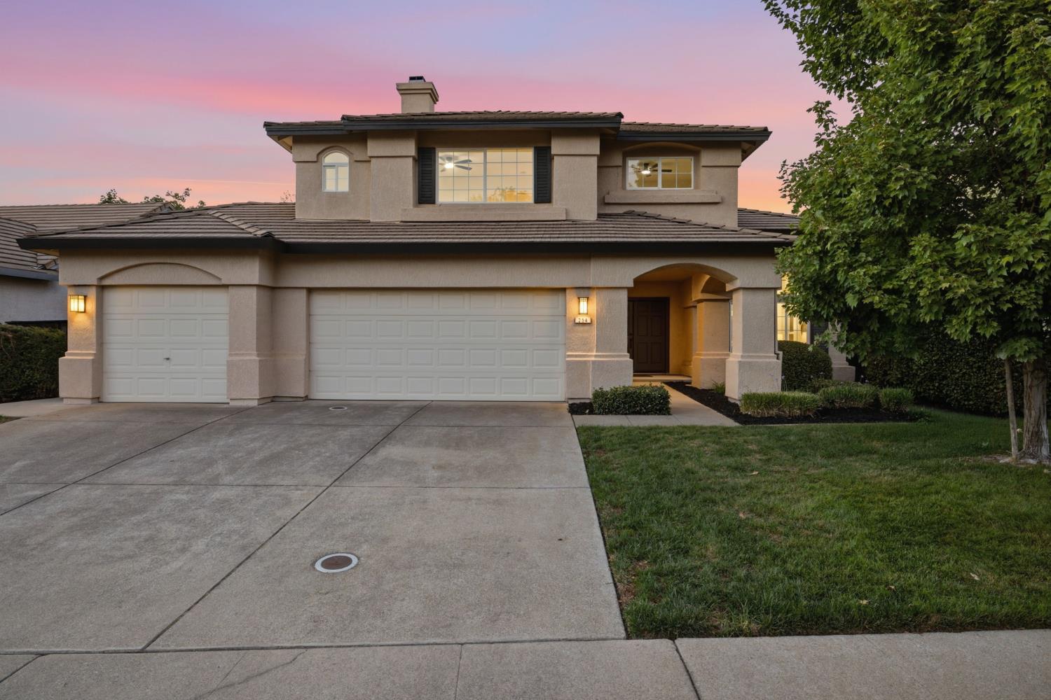 Two-story stucco home with a three-car garage and arched entry at dusk.
