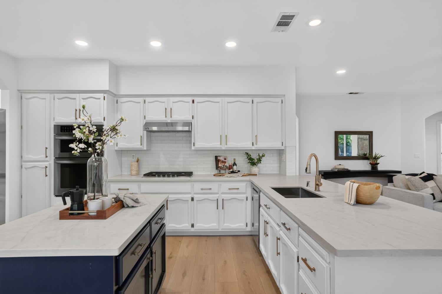 Open-concept kitchen with white cabinets, broad marble-look island, and brass faucet.