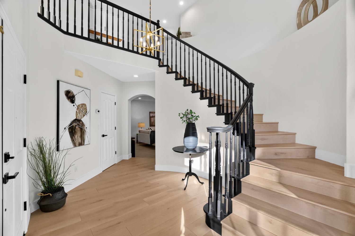 Entryway with a sweeping curved staircase, pale wood treads, and black railing.