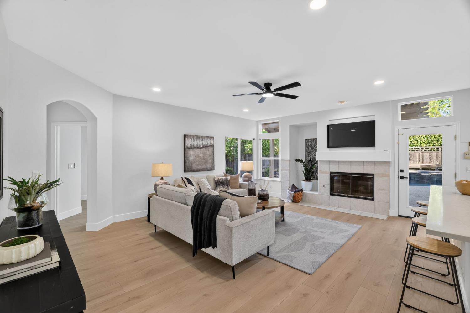 Living room with a gray sectional, tiled fireplace, and glass door overlooking the backyard pool.
