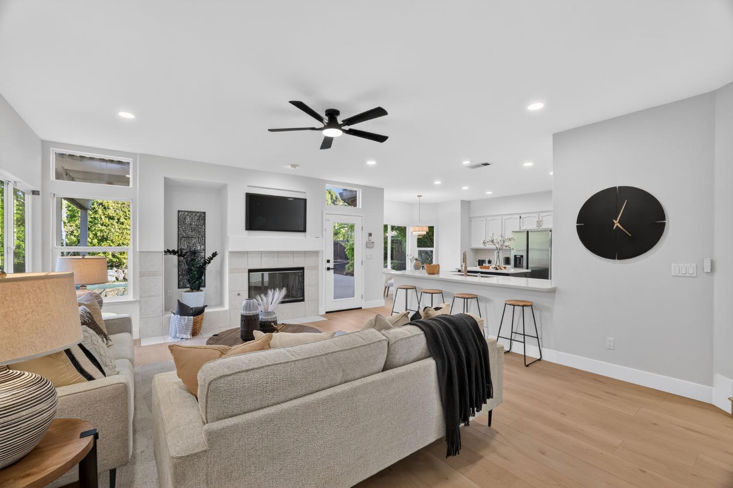 Open-plan living room with fireplace, neutral sofas, kitchen breakfast bar, and pool visible through the windows.