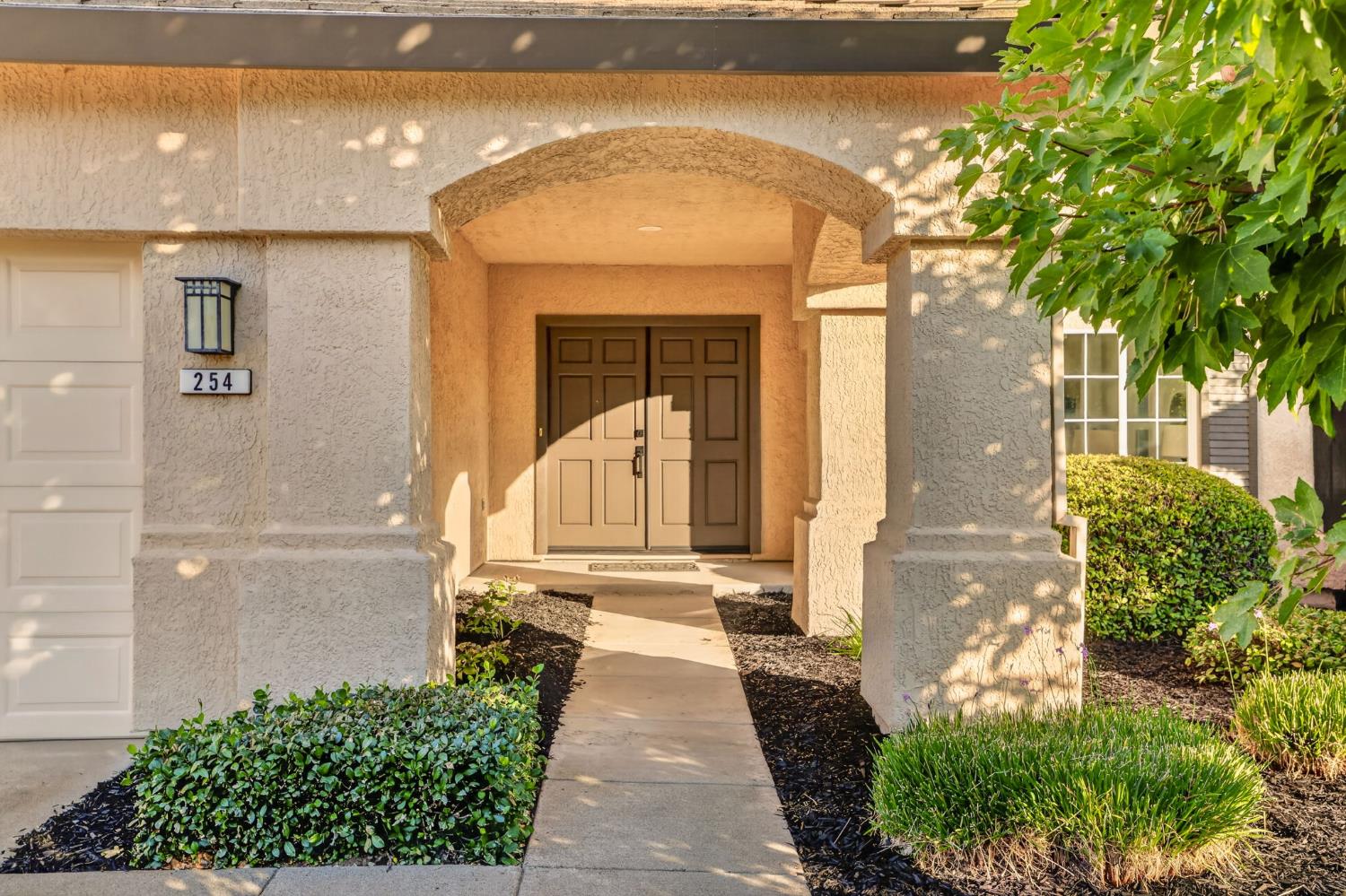 Stucco home entrance with an arched covered porch, double doors, landscaped walkway, and number 254.
