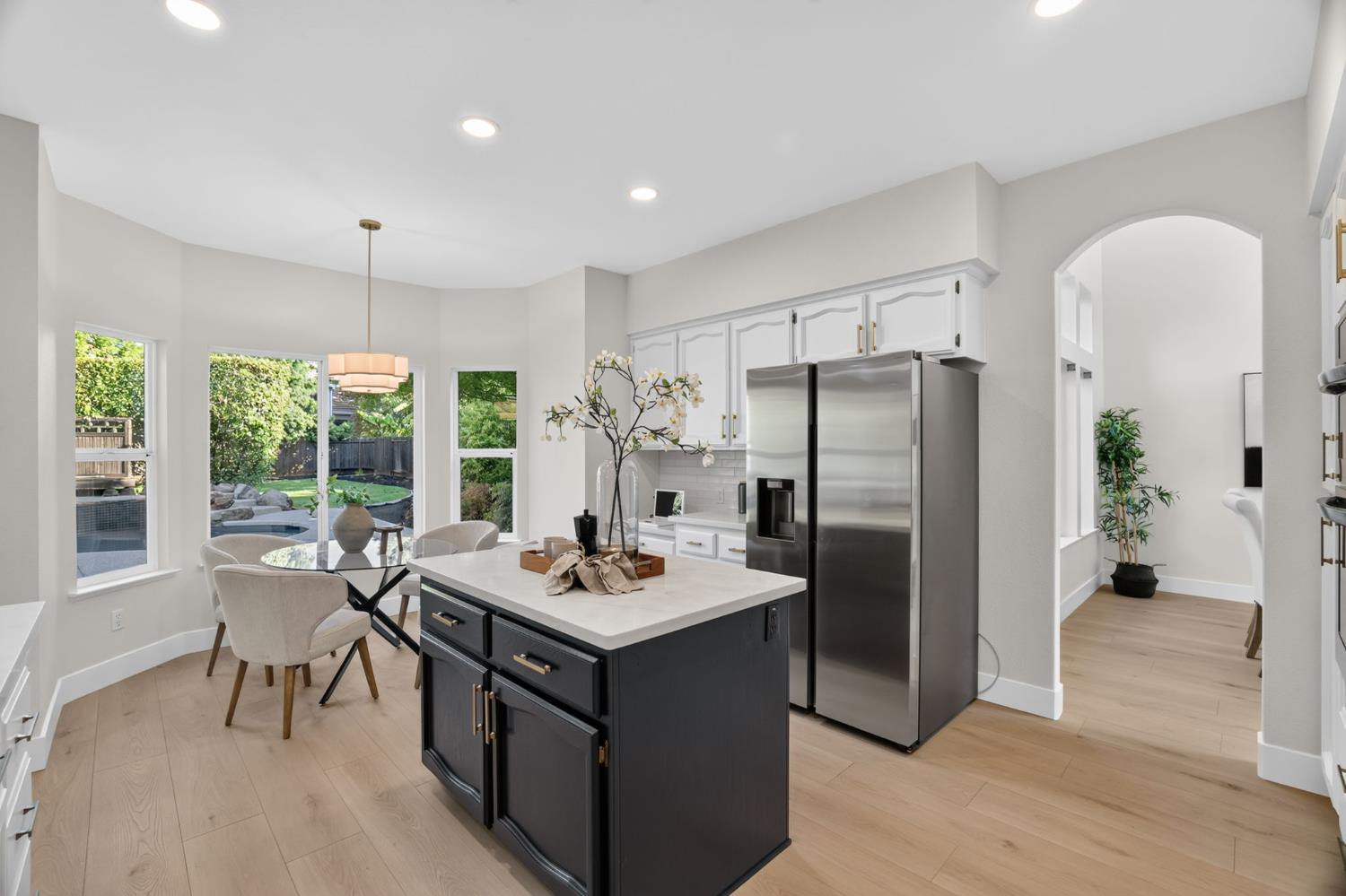 Bright kitchen with a dark island, stainless steel appliances, and a dining nook by backyard-facing windows.