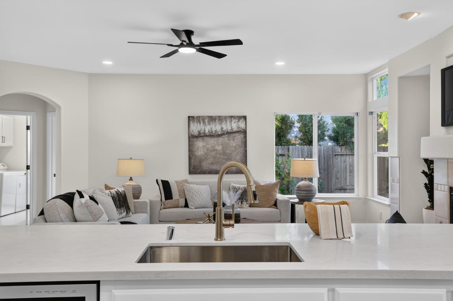 Kitchen island overlooking a furnished living room with large windows and a ceiling fan.