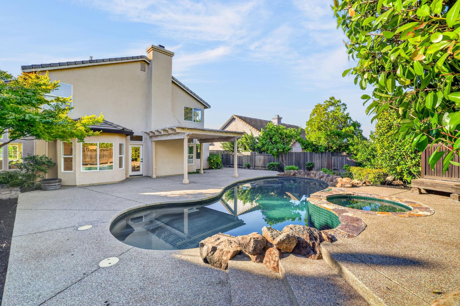 Backyard pool and raised stone-edged spa beside a two-story home and covered patio.