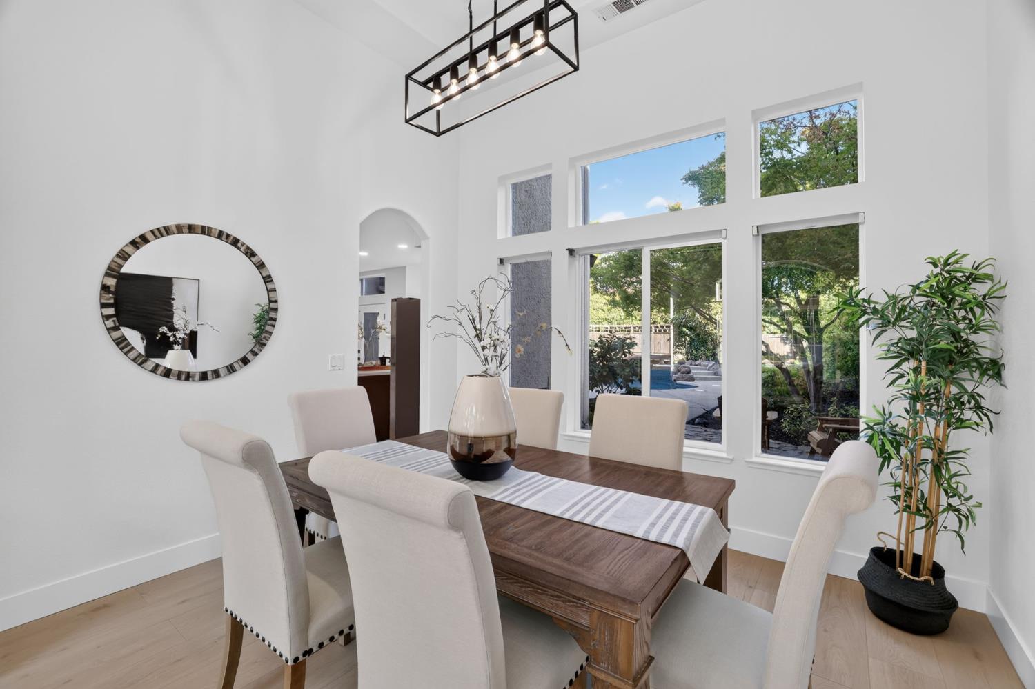 Dining room with a dark wood table, cream chairs, and tall windows overlooking the backyard pool.
