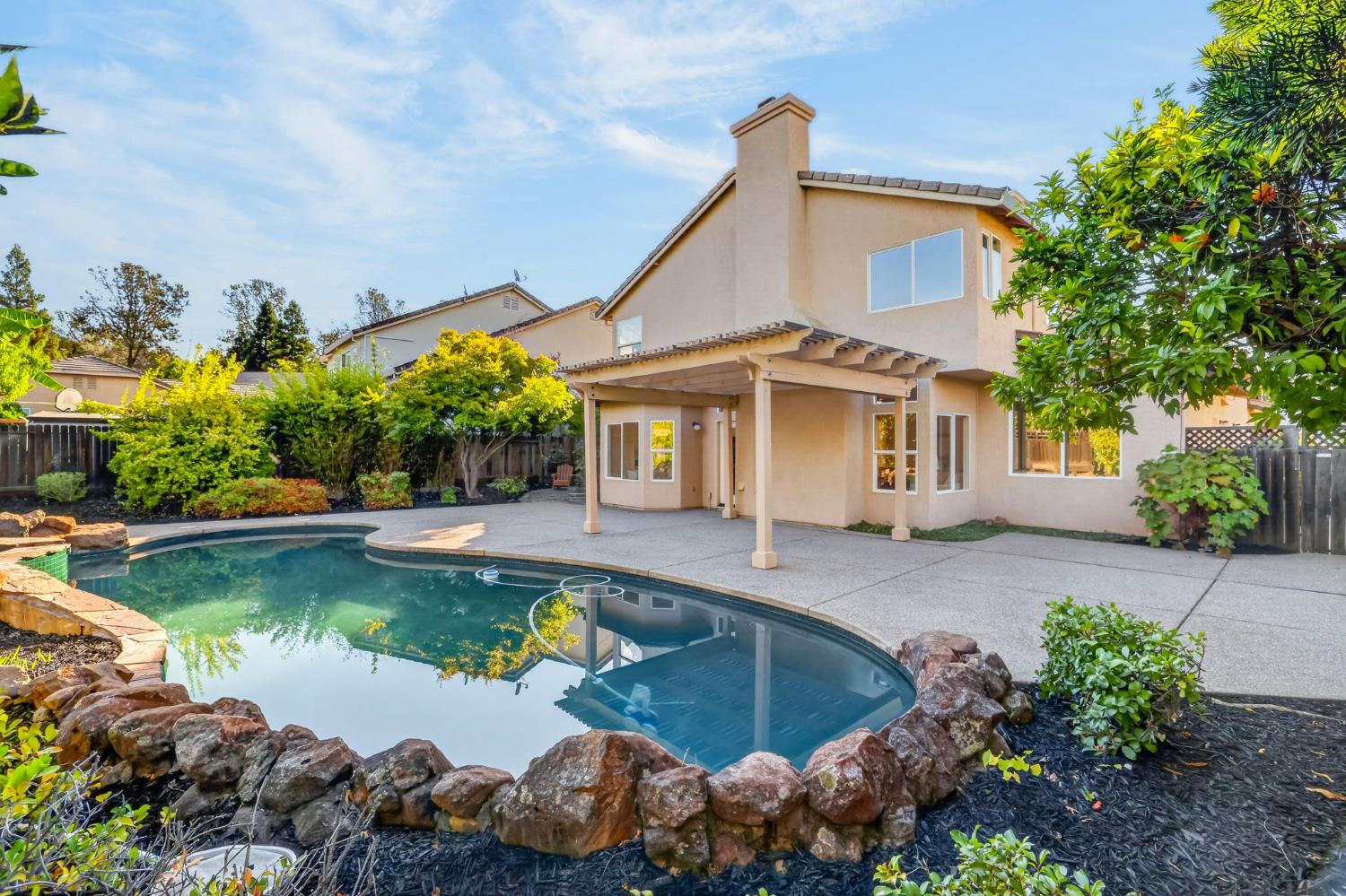 Two-story stucco home with a covered patio overlooking a curved, stone-edged swimming pool.