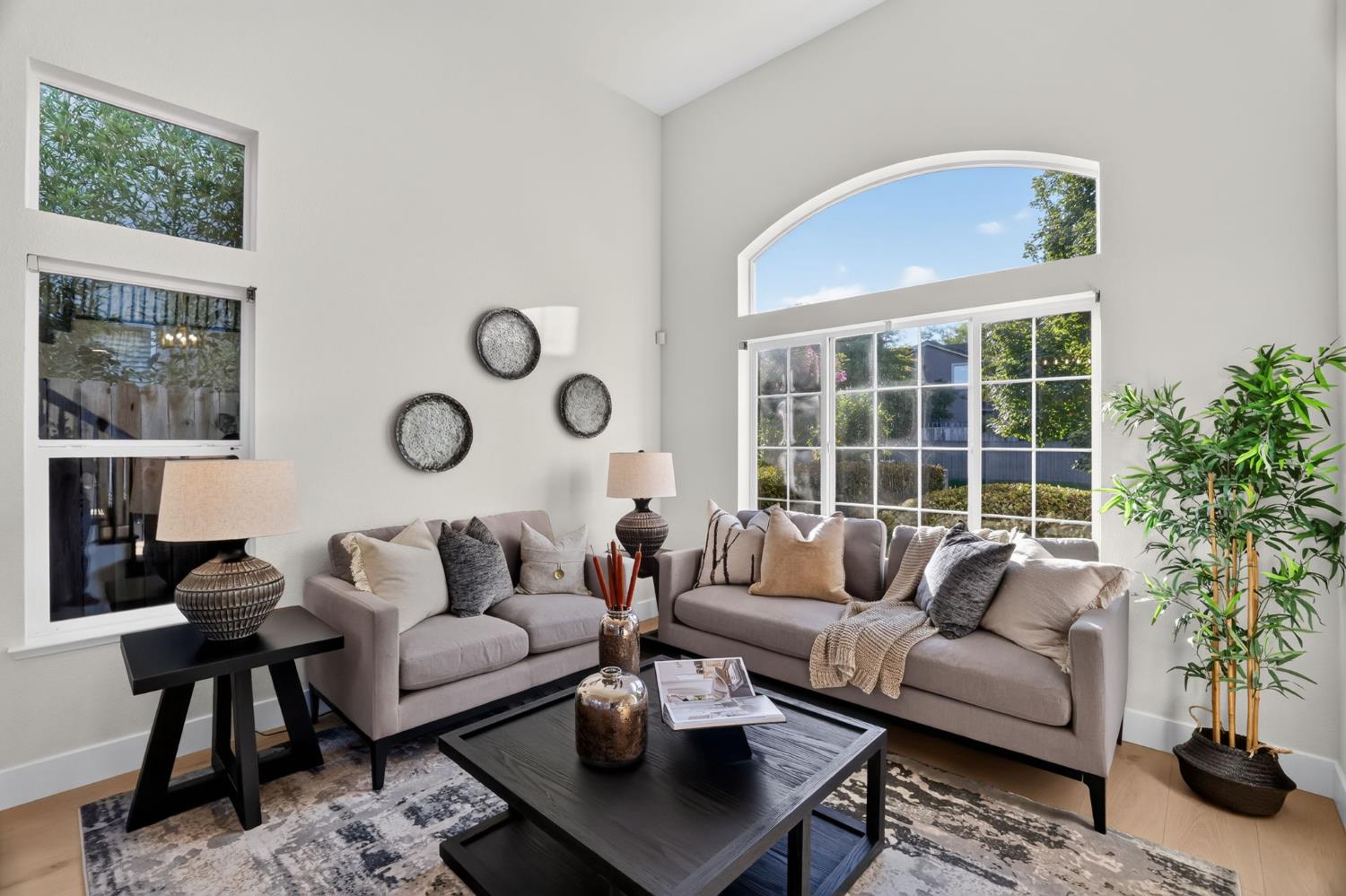 Staged living room with gray sofas, a dark coffee table, and a large arched window.