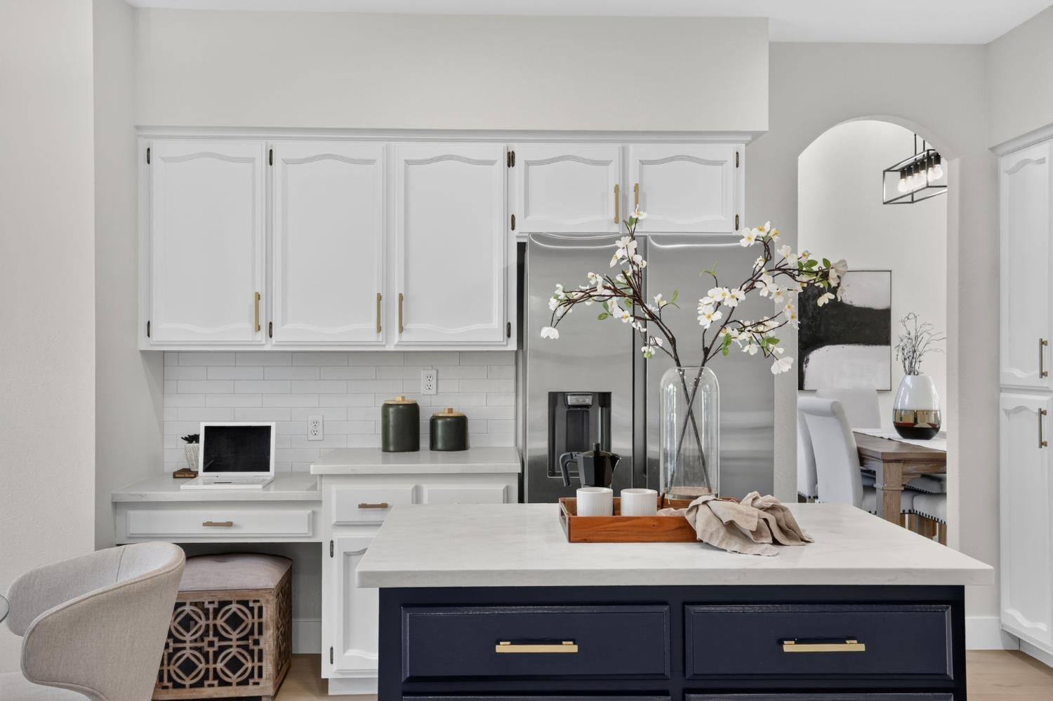 Kitchen with a navy island, white cabinets, and stainless-steel refrigerator; an archway opens to the dining area.