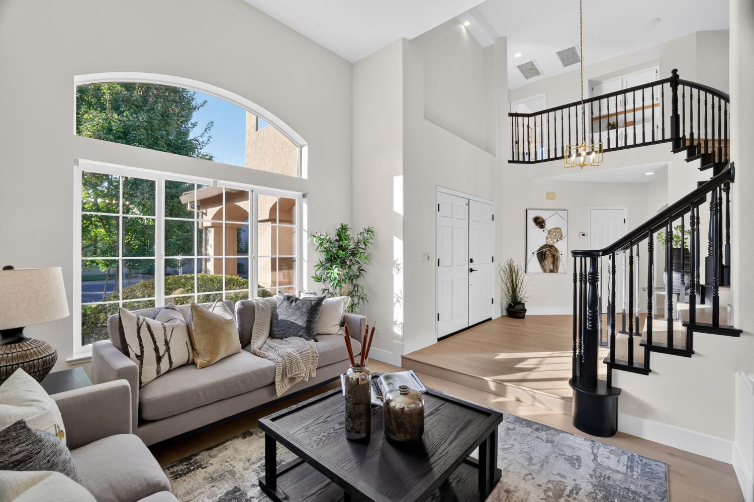 Furnished living room with vaulted ceilings, arched windows, and a black-railed staircase.