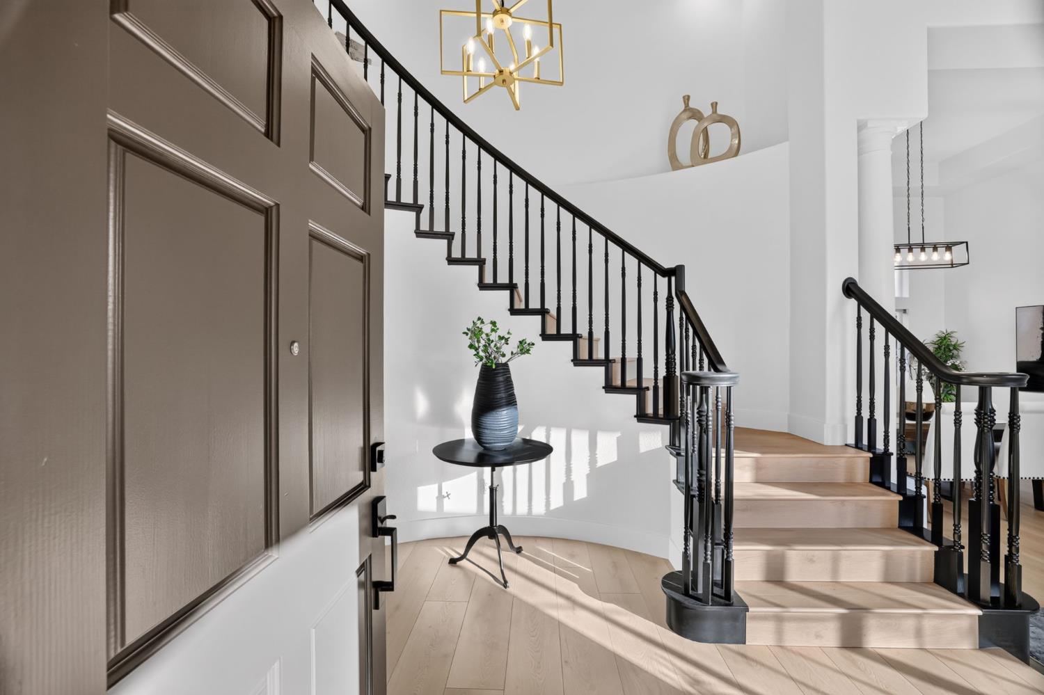 Entry foyer with a sweeping black-railed staircase, paneled front door, and geometric chandelier.