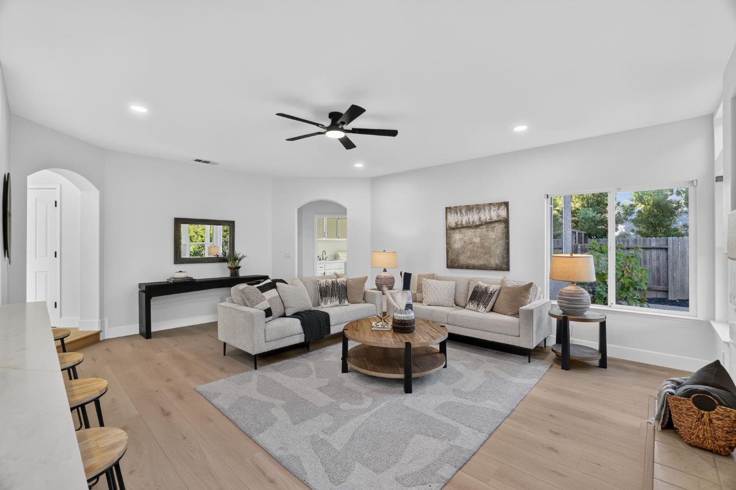 Staged living room with two sofas, a round coffee table, and large windows overlooking a fenced garden.