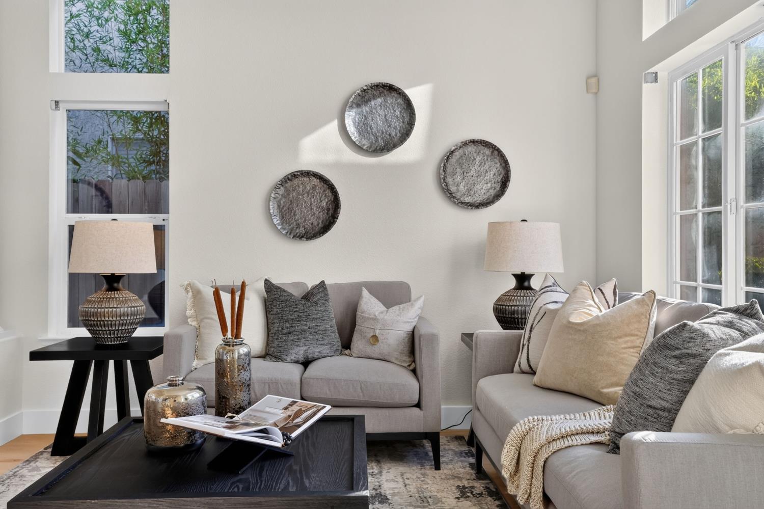 Staged living room with gray sofas, round wall decor, and tall windows.