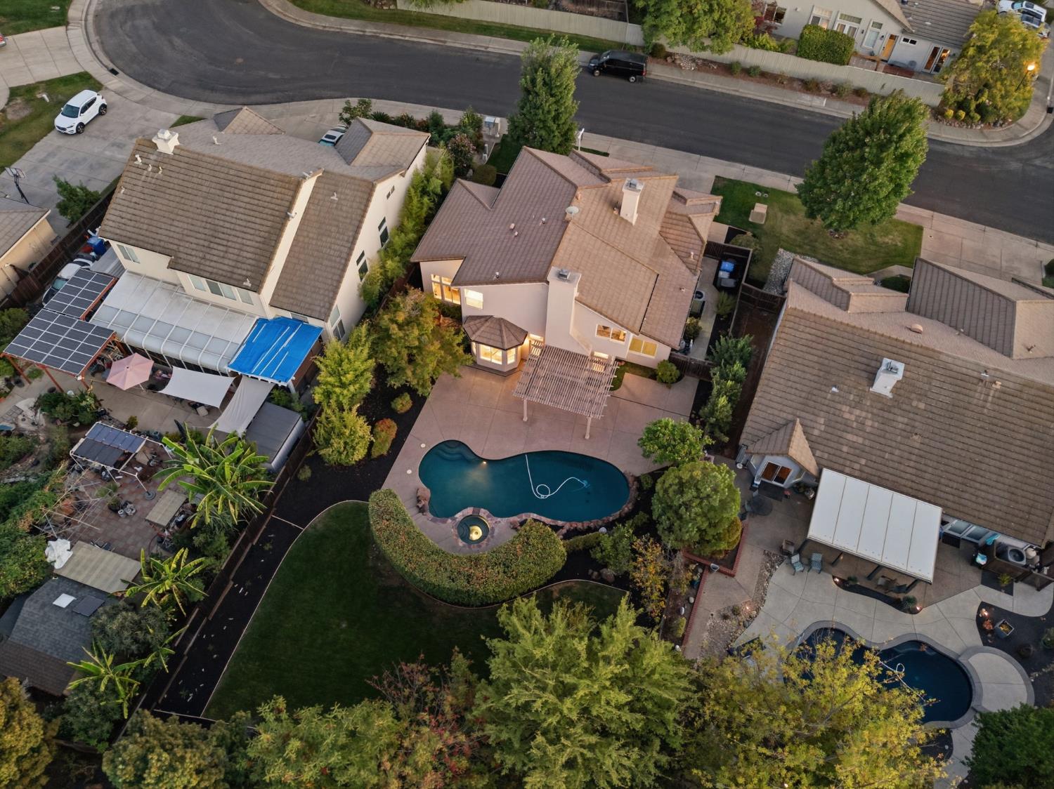 Aerial view of a home with a curved backyard pool, patio, and pergola.