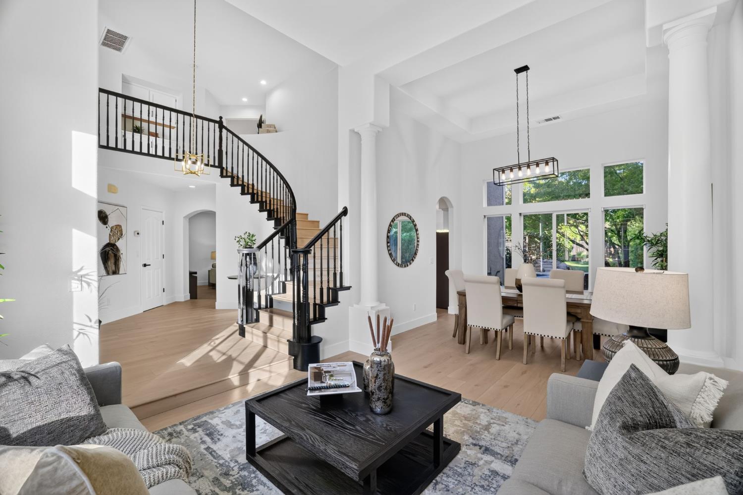 Open living and dining room with a curved staircase, tall ceilings, and large windows.