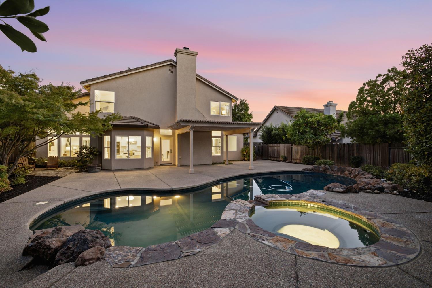 Two-story stucco home with a curved pool and raised stone spa at dusk.