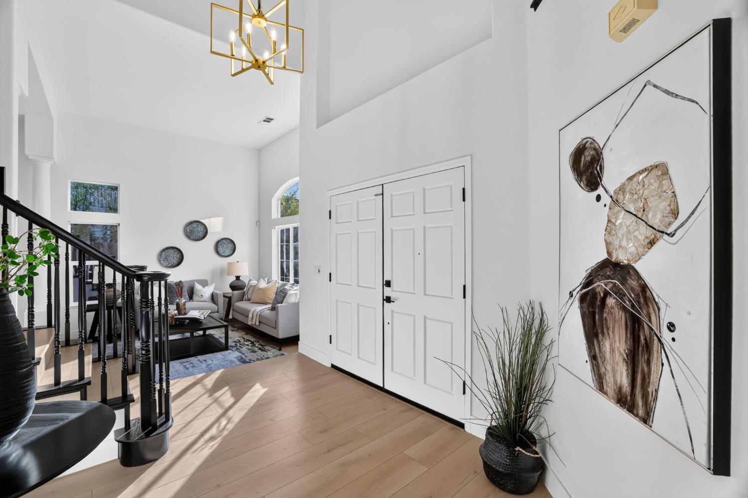 Bright entry foyer with white double doors, light wood floors, and a black staircase railing.
