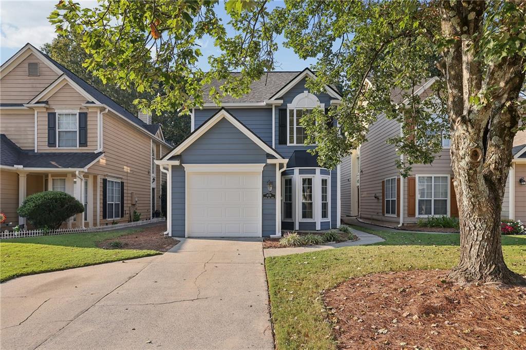 Blue two-story house with a white-trimmed garage, neighboring homes, and a large tree by the driveway.