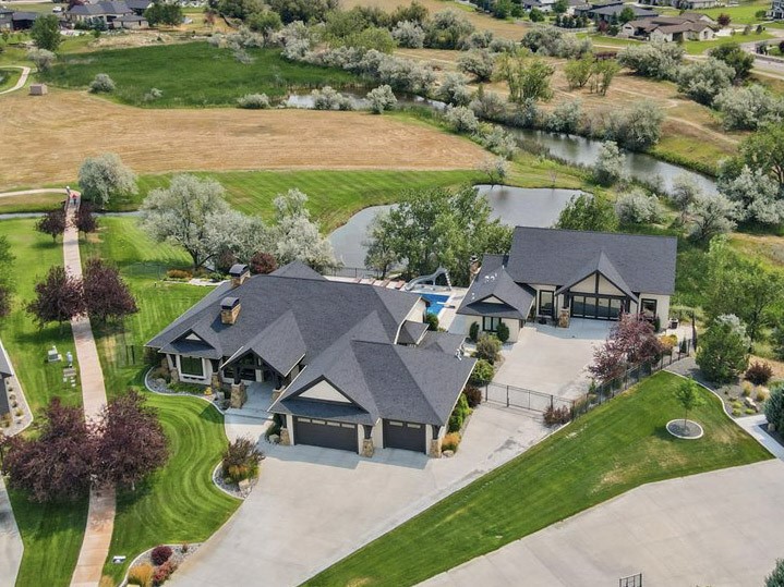 Aerial view of a large residence beside a pond, with landscaped grounds and a river beyond.