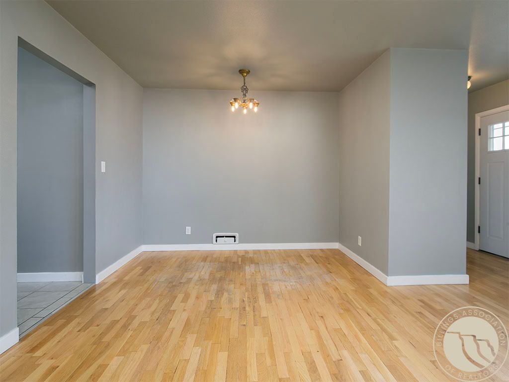 Empty dining room with light hardwood floors and a chandelier, adjoining a tiled area and entryway.